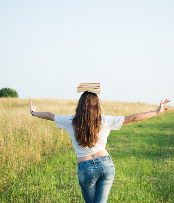 back of woman walking in a field balancing a stack of books on her head